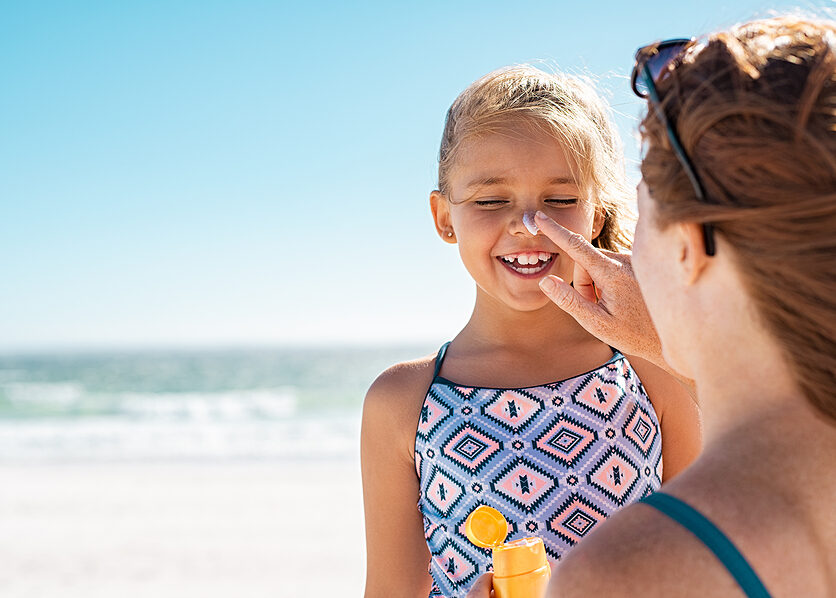 Young mother applying protective sunscreen on daughter nose at b Young mother applying protective sunscreen on daughter nose
