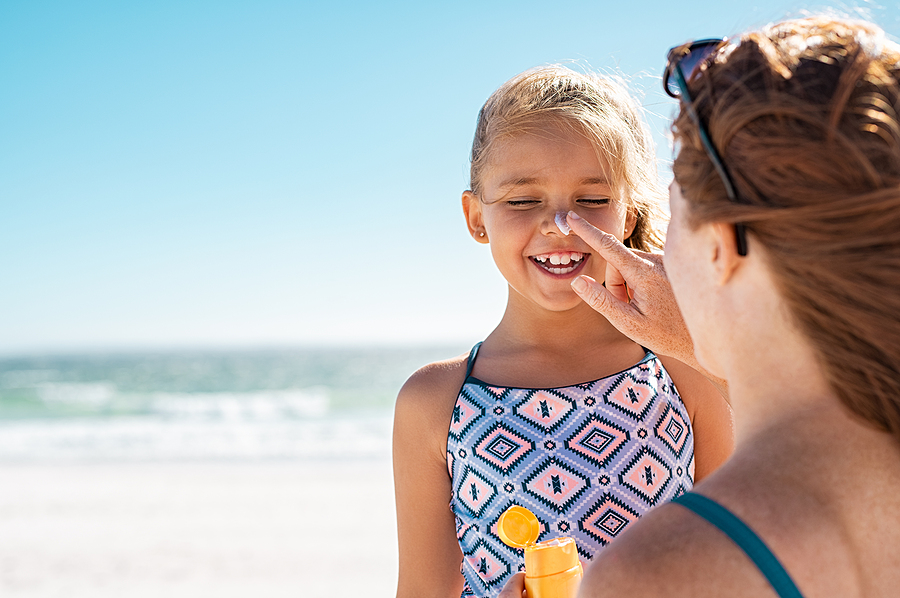 Young mother applying protective sunscreen on daughter nose