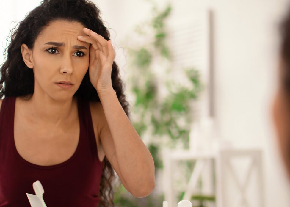 Unhappy Millennial Woman Looking At Her Reflection In Mirror, Ch dermatologist tips for dry skin